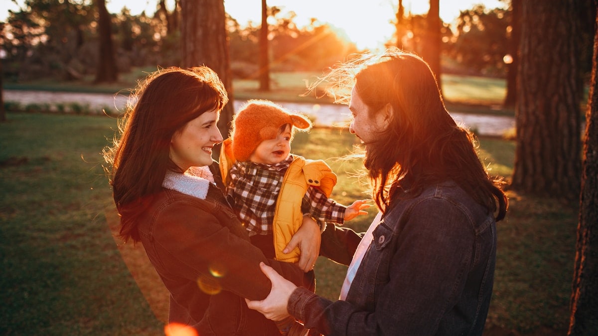 woman in black jacket carrying baby in white and black checkered dress shirt during daytime